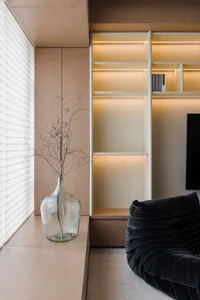 Modern living room with wooden cabinetry, glass shelves, and metallic accents.