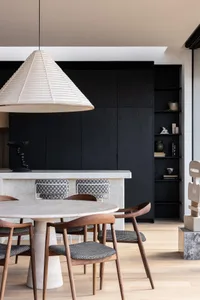 A modern dining room featuring a concrete table and chairs, with a large lampshade overhead and a black shelving unit in the 