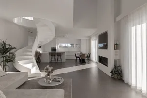 A modern living room featuring a white stone floor, a spiral staircase, a round coffee table, a minimalist sofa, and a kitche