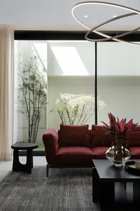 Minimalist modern living room featuring sleek, minimalist furniture with vibrant red cushions, large glass windows with natur
