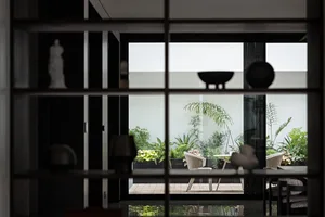View of a modern outdoor living space through a window, featuring glass walls and a wooden deck.