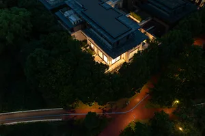 Aerial view of a modern residential building with concrete and glass materials, surrounded by greenery.