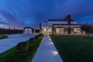 Modern residential exterior with concrete driveway, glass walls, and illuminated pathway.