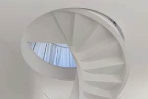 A white, minimalist, concrete staircase with a circular window in the ceiling.