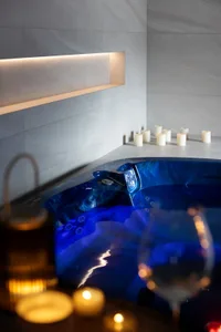 A spa setting with ceramic tile walls and a hot tub adorned with candles and wine glasses.