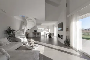 Modern, minimalist living room with white interiors, spiral staircase, and large windows.
