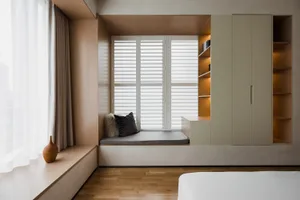 A minimalist bedroom with a wooden seating area by the window, featuring a cushion and a vase on the ledge, and a built-in bo