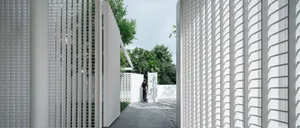 A minimalist white fence with geometric patterns and greenery in the background.