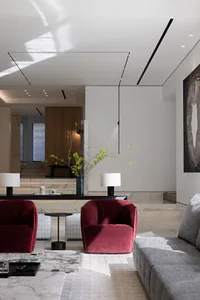 A modern living room with burgundy fabric armchairs, a gray sofa, and a marble coffee table.
