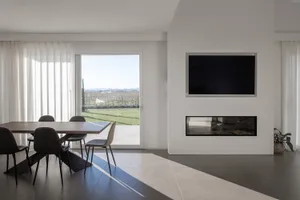 A modern minimalist living room with a concrete floor, a fireplace, a television, and a dining area with a wooden table and c