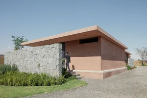 A minimalist exterior of a house with a pink sloped roof and concrete walls.