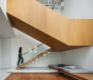 A modern minimalist residential interior with a wooden staircase, white walls, and a cushioned seating area.