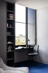 Modern minimalist home office with a built-in desk, black metal chair, and large window.