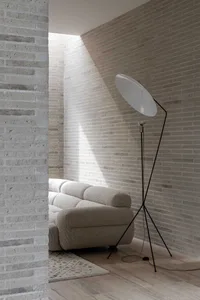 Modern minimalist living room with taupe fabric sofa and white floor lamp, featuring light brick walls and wooden flooring.
