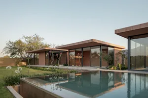 A modern residential house with a swimming pool made of concrete, surrounded by glass windows and metal structures.