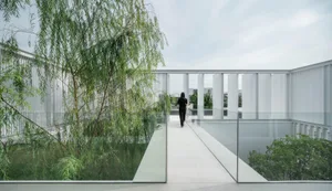 A modern rooftop patio with glass walls and a glass floor, featuring greenery and a person walking.