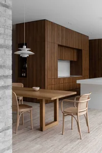 A modern minimalist kitchen featuring a wooden table and chairs, with dark wood cabinets and a white countertop.