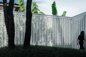 A minimalist exterior with a concrete lattice wall, trees, and greenery.