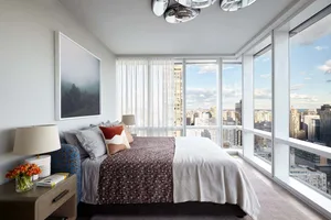 A modern bedroom featuring contemporary textiles, glass window frames, and a city view.