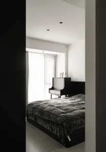 A modern bedroom with a black bed and grey blanket under bright sunlight from a large window.