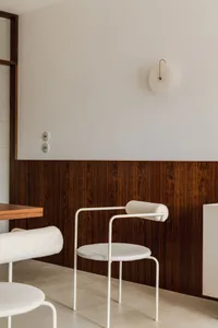 Modern dining room with wooden-paneled walls and contemporary white chairs.