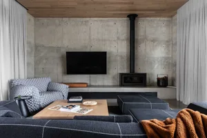 A modern living room featuring a concrete wall, leather armchair, fabric sofa, and a coffee table with a bowl and book.