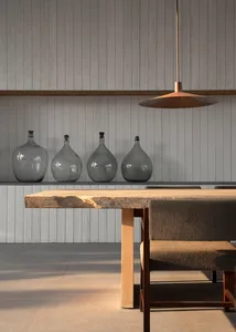 Minimalist, industrial dining room featuring a large wooden table, four dark glass bottles on a ledge, and a brass pendant li
