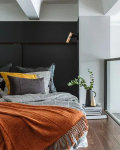 Minimalist bedroom featuring a bed with a dark headboard and mixed texture bedding, along with a small plant on a stack of bo