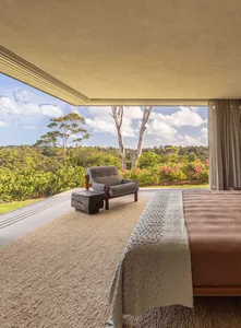 A minimalist bedroom featuring neutral colors and a view of lush greenery outside.