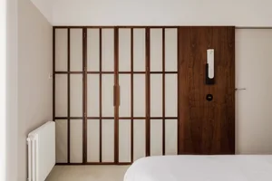 A minimalist bedroom with a white bed and a dark wooden closet with frosted glass doors.