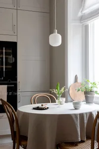 A minimalist dining space with neutral-toned furniture and decor, featuring a round wooden table, wooden chairs, and a hangin
