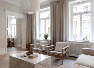 A minimalist living room with neutral-toned furniture and decor, featuring a white marble coffee table, wooden chairs, and la