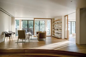 Modern minimalist living room with wooden flooring, chairs, and shelves.