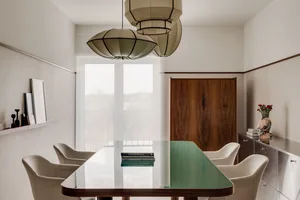 A contemporary dining room with a glass table, wooden cabinet, and fabric chairs.