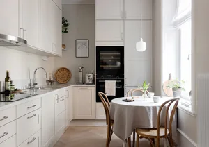 A minimalist white kitchen with a round table and chairs by the window.