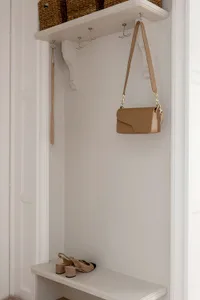 A minimalist white storage space with a bench, hooks, and a bag hanging.