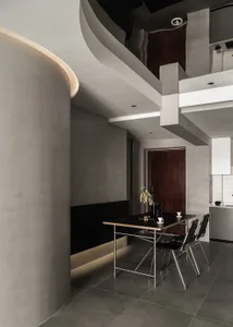 A modern dining room featuring a minimalist table and chairs, set against a backdrop of concrete walls and floors.