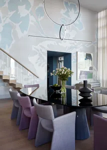 A modern dining room with a glass table, purple and gray chairs, and abstract art on the wall.