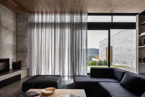 A modern living room with concrete walls, glass elements, and upholstered furniture.