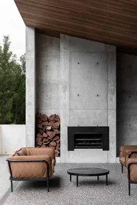 A modern living space with a concrete wall, a black fireplace insert, and brown upholstered armchairs.