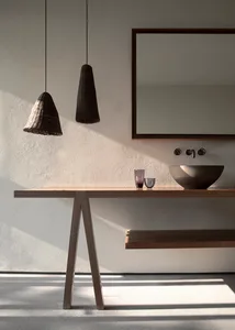 A modern minimalist bathroom with a wooden table and floating shelves, a black woven pendant light, and a sink with a bowl-sh