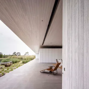 An image of a minimalist, modern residential outdoor space with a concrete floor and walls, featuring a single natural woven 