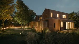 A modern residential home with a brick exterior, illuminated at night, surrounded by a well-lit garden.