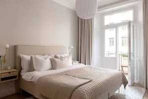 A minimalist bedroom featuring a bed with fabric bedding and wooden furniture, natural light streaming through the window.