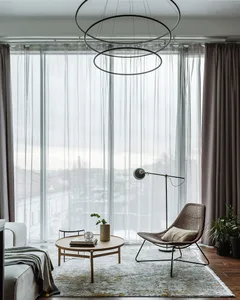 A modern minimalist living room with transparent curtains, a round wooden coffee table, a floor lamp, and a potted plant.