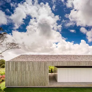 A modern house with a bamboo cladding exterior under a cloudy blue sky.