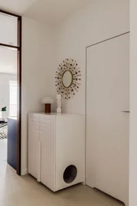 A modern white entryway cabinet with a sunburst mirror and a simple lamp.