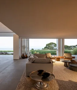 A modern living room with a concrete floor, featuring minimalistic furniture and a view of the ocean.