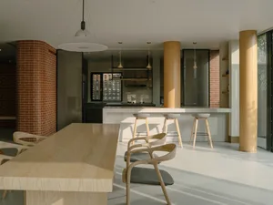 A modern residential kitchen featuring minimalist design, wood, concrete, and brick materials, with a long dining table and b