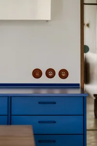 Close-up of a blue dresser with three brass light switches against a white background.